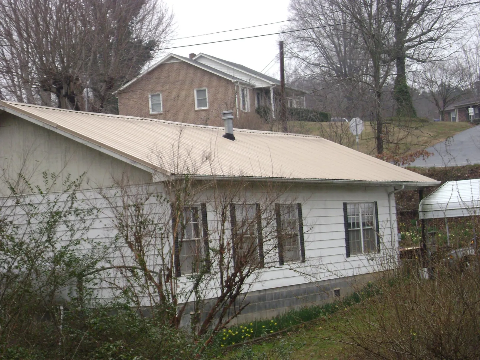 Tan metal roof on a white sided house set into a hillside — Commercial Roofing by Roofing Brothers in Chichester
